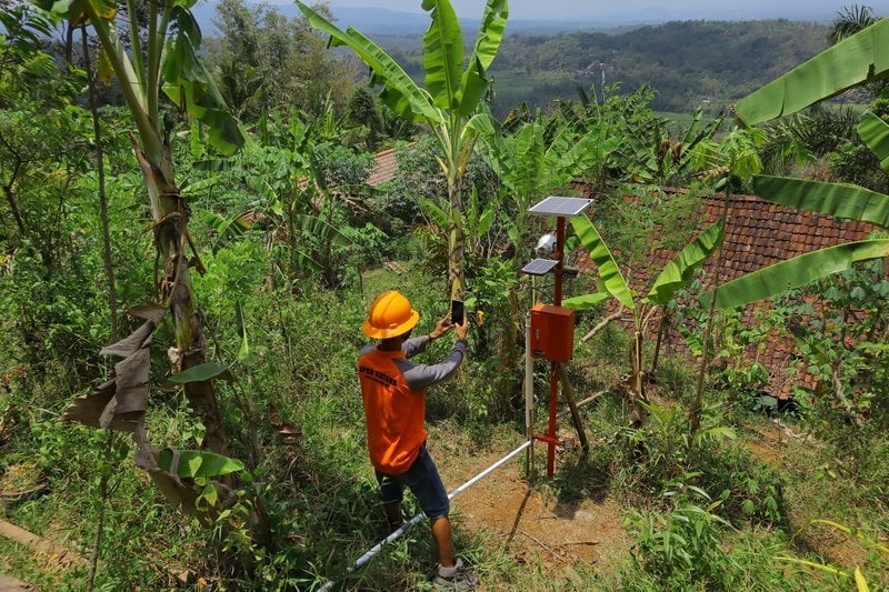 Worker uses a smartphone to document the condition of the solar panel for a landslide early warning system on a rural hill slope near Magelang, Indonesia.